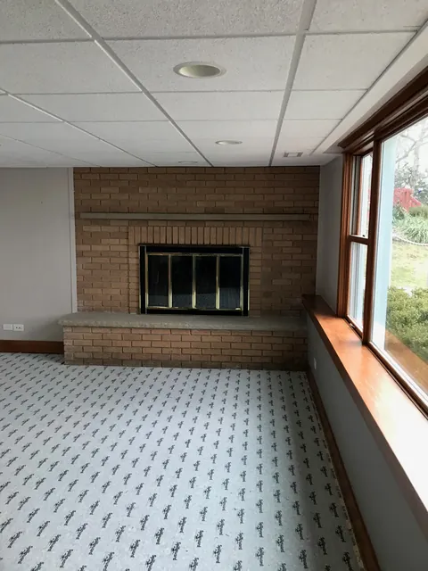 A red brick fireplace with brass-trimmed glass doors and a raised brick hearth, before the work.