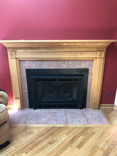 The same oak mantel and tile, now holding a black gas insert with a log set behind the glass.
