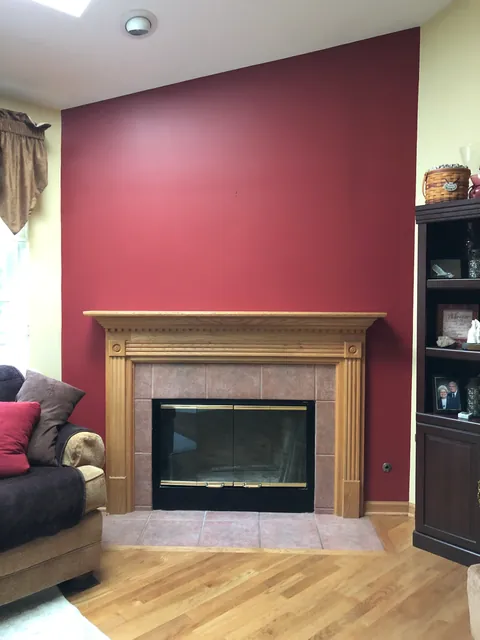 A fireplace with brass-trimmed glass doors and a tile surround, set in an oak mantel against a red accent wall.