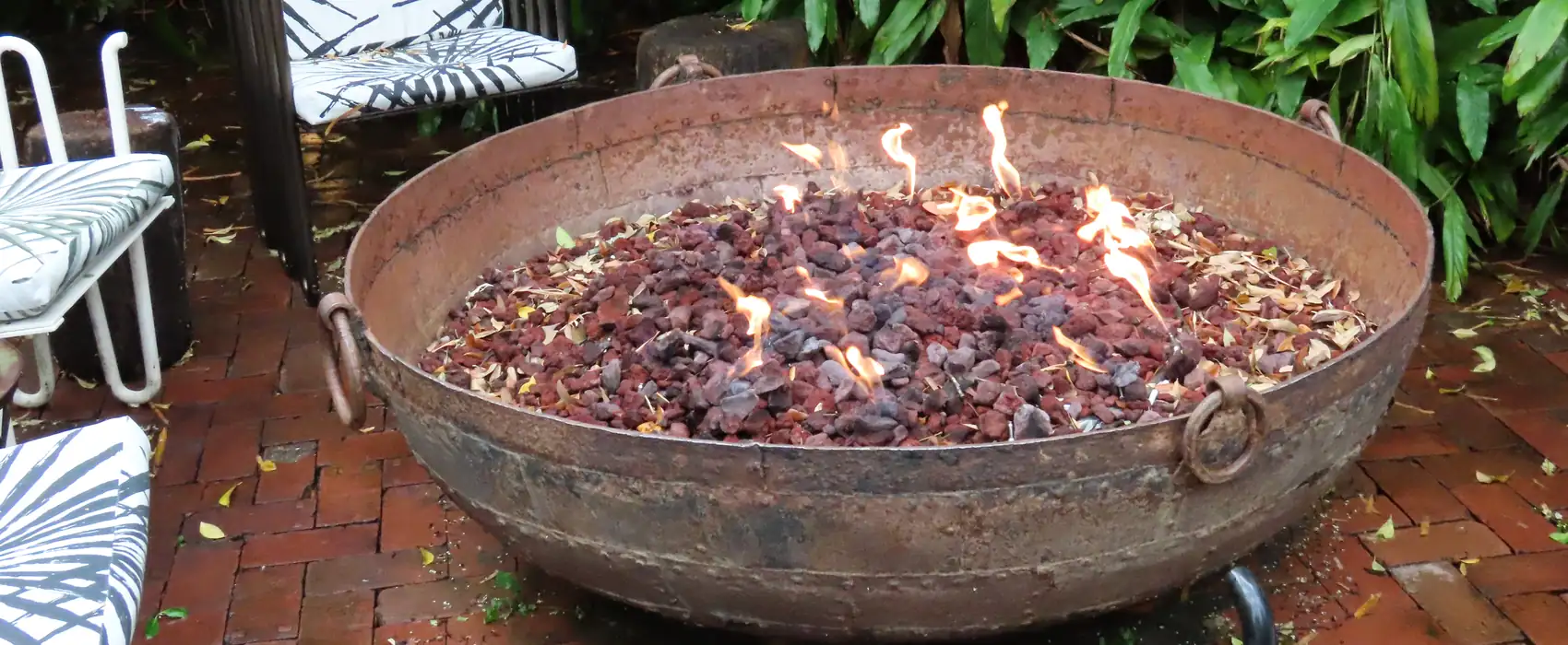 A wide fire bowl full of glowing coals on a brick patio.